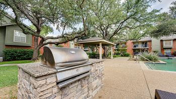 A BBQ grill is on a stone pillar in a courtyard.